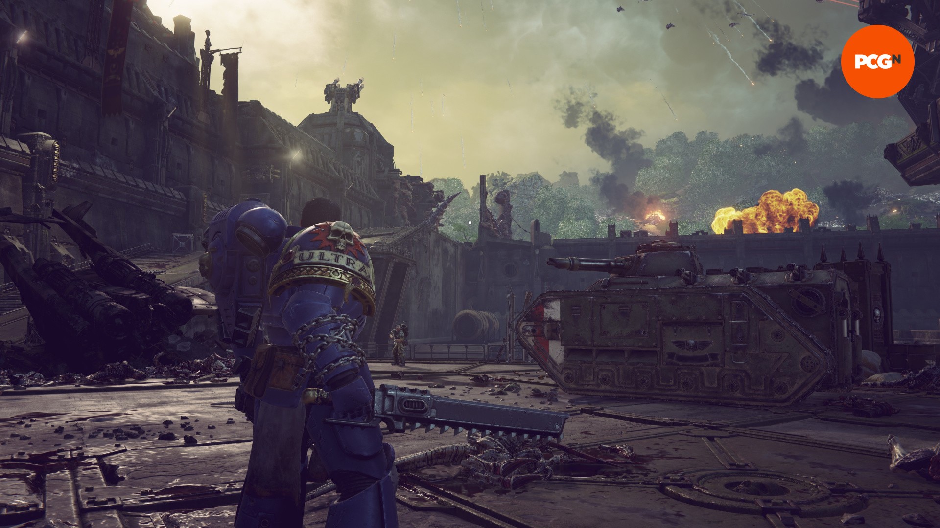 Space Marine 2 review: A man in blue armor stands in front of a large war tank, from Space Marine 2.