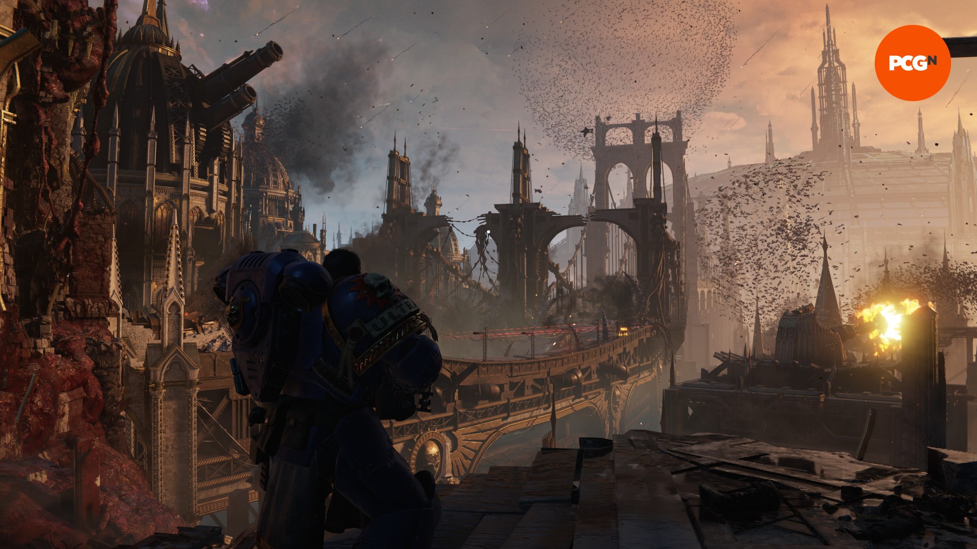 Space Marine 2 review: A man in blue armor stands in front of a destroyed city of gothic buildings, from Space Marine 2.